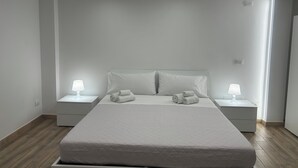 A modern bedroom with a large bed, two bedside tables with lamps, and a wooden floor. - At 100 mt from the sea and train station, rooms with all amenities (Nettuno)