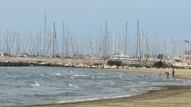 A beach with a row of sailboats docked behind a rocky breakwater. - At 100 mt from the sea and train station, rooms with all amenities (Nettuno)