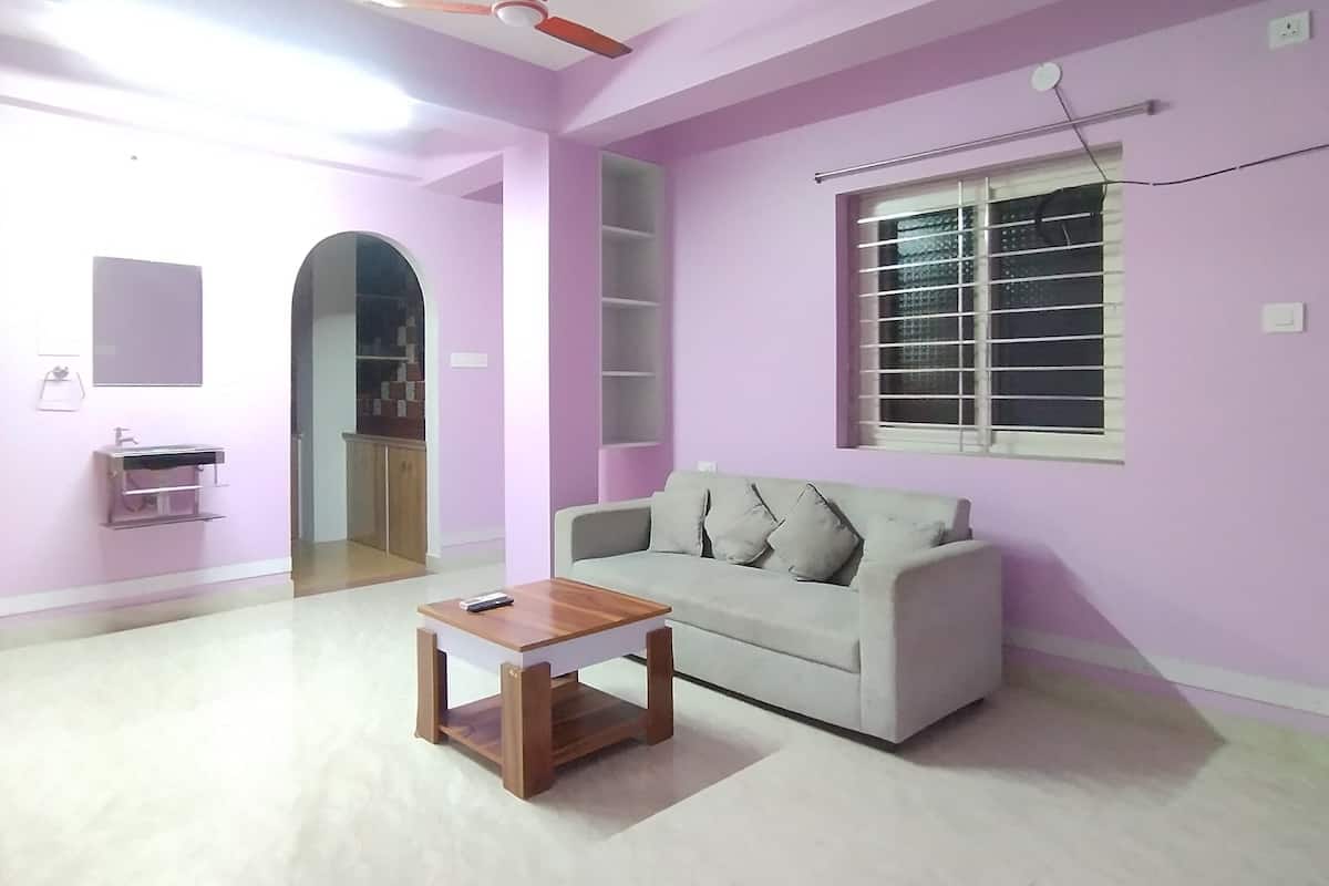 A living room with a white sofa, a wooden coffee table, a ceiling fan, a window with blinds, and a pink wall.