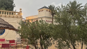 An outdoor seating area with red chairs and tables, a palm tree, and a building with a tower labeled "Anberg."