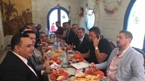 Una lunga tavola da pranzo con diverse persone sedute, circondata da piatti e cestini di pane.