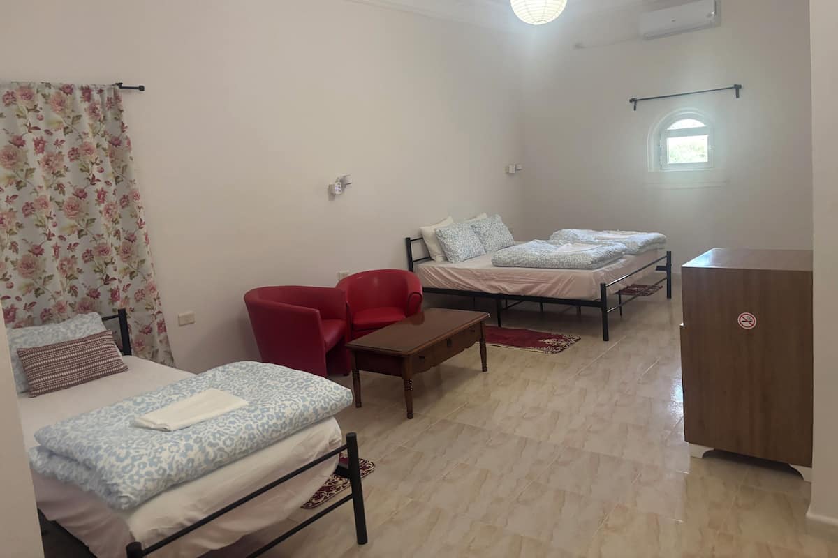Une chambre avec deux lits, une chaise rouge, une table en bois et une armoire.
