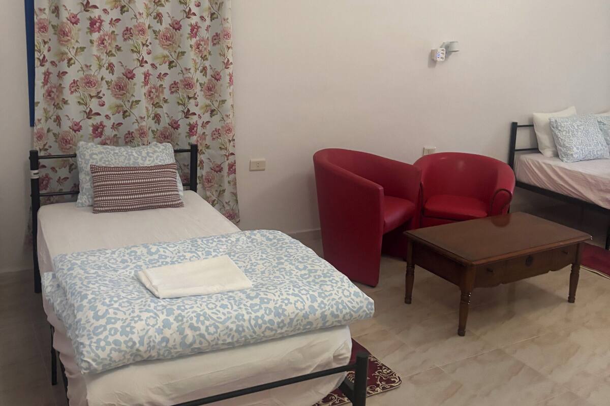 Une chambre à coucher avec un lit, une chaise rouge, une table en bois et un rideau à motifs floraux.