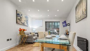 A modern living room with a glass dining table, a sofa, and a TV mounted on the wall. - Mill Conversion Flat Mins from Printworks - Pass the Keys (Salford)