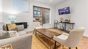 A modern living room with a sofa, armchairs, a coffee table, and a television mounted on the wall. - Mill Conversion Flat Mins from Printworks - Pass the Keys (Salford)