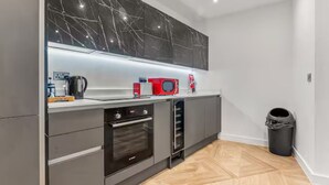 A modern kitchen with grey cabinets, a black marble backsplash, a red microwave, and a coffee machine. - Mill Conversion Flat Mins from Printworks - Pass the Keys (Salford)