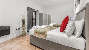A modern bedroom with a large bed, a flat-screen TV, a plant, and a grey sofa. - Beautifully 3Bed Restored Apartment near Deansgate - Pass the Keys (Salford)