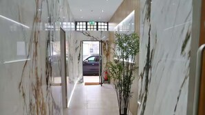 A hallway with marble walls, a potted plant, and a car visible through the doorway. - Beautifully 3Bed Restored Apartment near Deansgate - Pass the Keys (Salford)