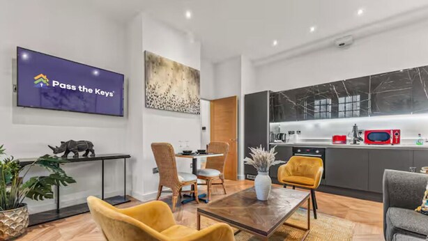 A modern living room with a dining area, a kitchen, and a mounted television displaying 'Pass the Keys'. - Beautifully 3Bed Restored Apartment near Deansgate - Pass the Keys (Salford)