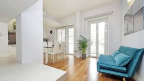 Ein modernes Wohnzimmer mit einem türkisfarbenen Sofa, Holzböden und einem Essbereich mit weißen Stühlen.