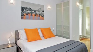 Ein Schlafzimmer mit einem Bett, zwei Kissen, einem Nachttisch, einem Wandbild und einem Schrank mit Glastüren.