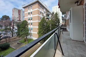 Ein Balkon mit Blick auf ein mehrgeschossiges Gebäude, einen Parkplatz und Bäume.