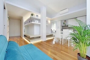 Un espace de vie moderne avec un canapé bleu, un plancher en bois, des meubles blancs et une plante en pot.