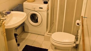 Et lille badeværelse med vaskemaskine, toilet, håndvask og brusekabine i glas.