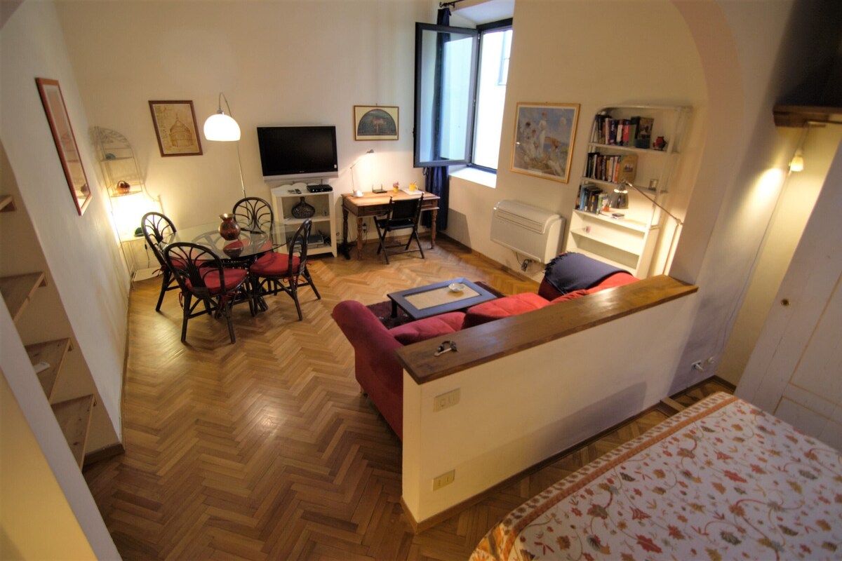 Un espacio habitable compacto con un sofá, una mesa de comedor con sillas, un televisor y una estantería.