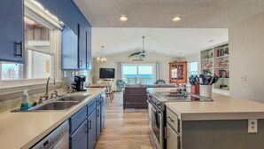 A modern kitchen with a central island, built-in appliances, and a large window overlooking a balcony. - Beachy McBeach House: Bold, Bright & Beachy (Surf City)