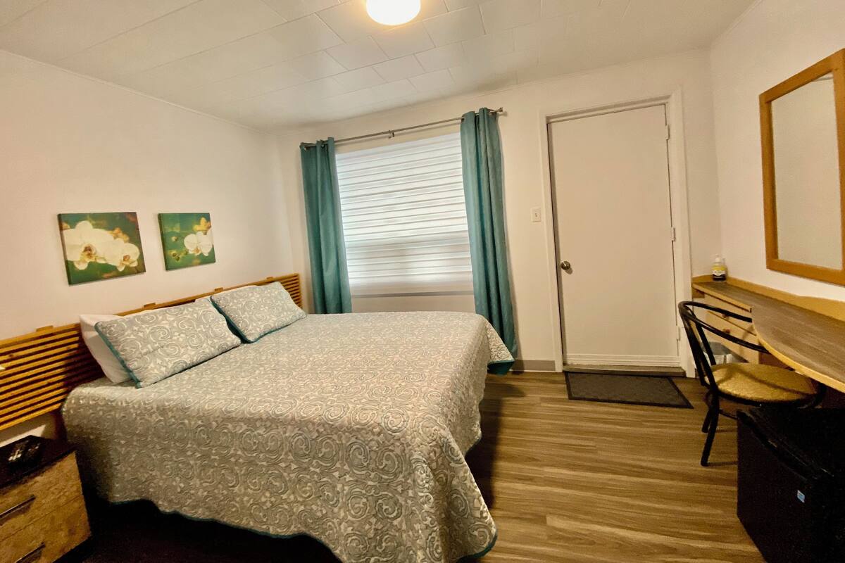 A bedroom with a bed, a desk, and a chair. There are two paintings on the wall.