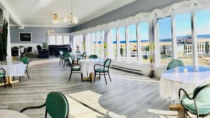 Un comedor amplio con ventanas grandes que ofrecen vistas a la playa. Las mesas y sillas están dispuestas para comer.