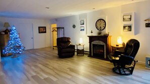 Una sala de estar con piso de madera, chimenea, un reloj y un árbol de Navidad.