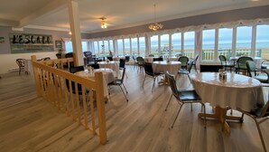 Un restaurante con mesas redondas, sillas y vista al mar.