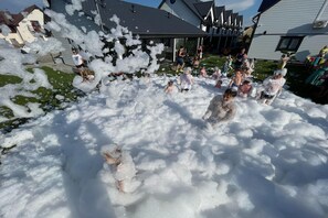 En gruppe mennesker leger med skum i et udendørs område med huse i baggrunden.
