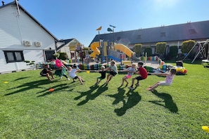 A group of children playing tug-of-war on a grassy field with playground equipment in the background.