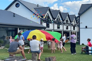 Un groupe de personnes joue avec un grand parapluie coloré devant un bâtiment doté de plusieurs toits à pignons.