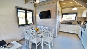 A compact kitchen with white cabinetry, a built-in washing machine, and a dining area with white chairs and a table set for two. - Holiday homes close to the beach, air conditioning (Sianozety)