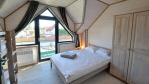 A bedroom with a sloped ceiling, a bed with white bedding, a wardrobe, and a window with curtains. - Holiday homes close to the beach, air conditioning (Sianozety)