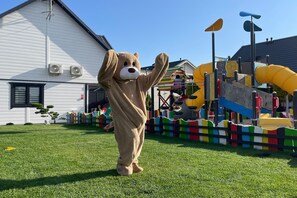 Eine Person in einem Bärenkostüm steht vor einem Haus mit einem Spielplatz.