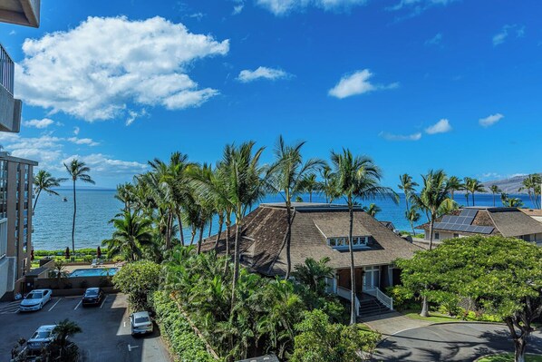 A residential area with a view of the ocean, palm trees, and a house with a sloped roof. - 2BR Kihei condo w/ pool and sunset views (Kihei)