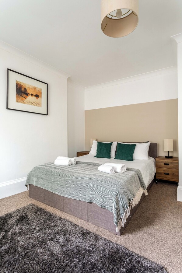 A neatly arranged bedroom with a bed, a bedside table, a lamp, and a framed picture on the wall. - Super Central 3 Bed Property (Brighton)