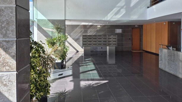 Eine moderne Lobby mit Glaswand, einer Rezeption und einem Bereich mit Pflanzen.