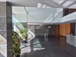 A modern lobby with a glass wall, a reception desk, and a plant area. - Lisbon - central, modern, with balcony, two suites, garage and security  (Lisboa)
