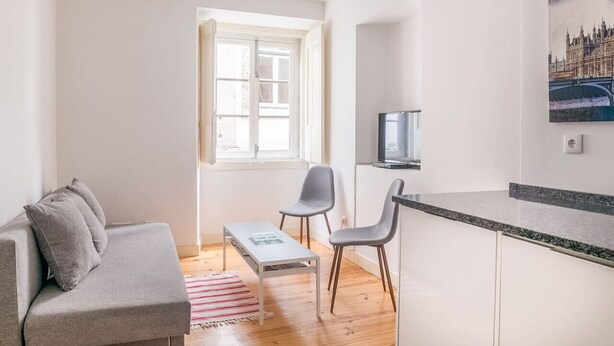 Un espacio habitable compacto con sofá, dos sillones, una mesita, televisor y zona de cocina con mostrador.