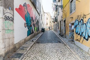 Una estrecha calle adoquinada con edificios a ambos lados, uno con un mural y otro con grafitis.