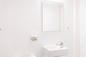 A bathroom with white tiles, a white sink, a mirror, and a soap dispenser.