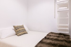 A bedroom with a bed, a patterned pillow, a fur throw, and a white shelf unit.