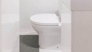 Un baño moderno con inodoro blanco, lavabo con espejo y zona de ducha.