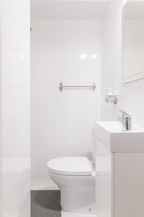 Un baño moderno con inodoro blanco, lavabo con espejo y zona de ducha.