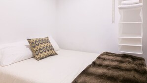 Un dormitorio con cama, un cojín estampado, una manta de piel sintética y un mueble blanco.