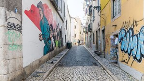 Una estrecha calle adoquinada con edificios a ambos lados, uno con un mural y otro con grafitis.