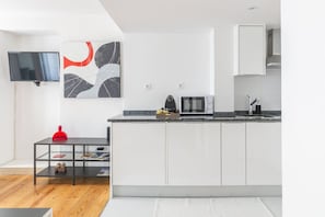 Una cocina moderna con armarios blancos, encimera negra y televisor de pantalla plana montado en la pared.