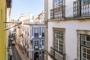 A narrow street with buildings featuring traditional architecture, including balconies with wrought iron railings and a mix of window styles.