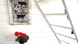 Ein Essbereich mit kariertem Tischlein, roter Geschirrdekor, einem gerahmten Bild und einer Vase mit roten Blumen.