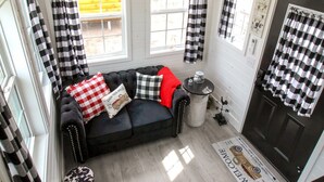 Ein gemütliches Blockhäuschen-Interieur mit einem schwarz-weißen Schachbrettsofa, einem kleinen runden Tisch und einer Fußmatte.
