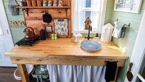 Una cocina con estantes de madera, un hervidor, un lavabo y una ventana con cortinas.
