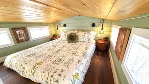 Un dormitorio con techo de madera, colcha estampada y luces fijadas a la pared.