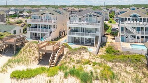 A beachfront residential area with multi-story houses featuring balconies, a swimming pool, and a beach access deck. - Sun Realty stunning oceanfront Nags Head vacation home with elevator! (Nags Head)