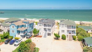 A coastal residential area with multi-story houses, a beach, and a pier. - Sun Realty stunning oceanfront Nags Head vacation home with elevator! (Nags Head)